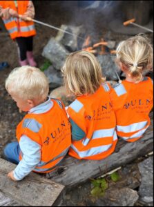 Barn i refleksvester griller pølser over bål